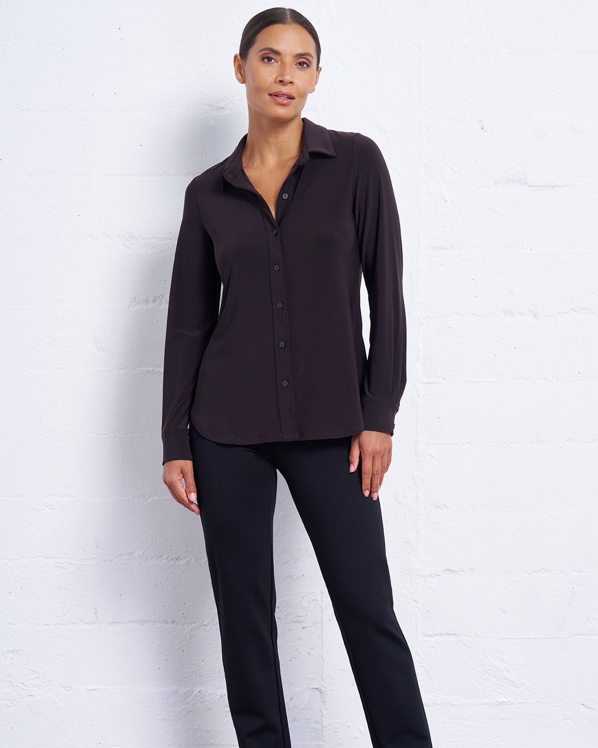Woman wearing a black shirt and pants against a white brick wall.