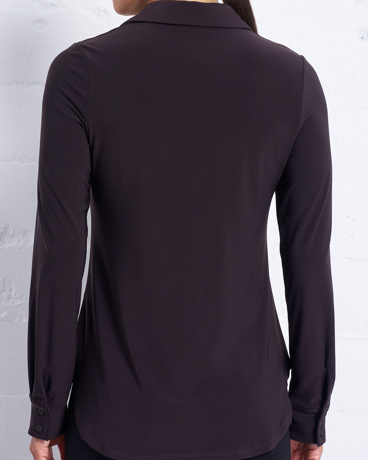 Black shirt worn by a person against a white brick wall.